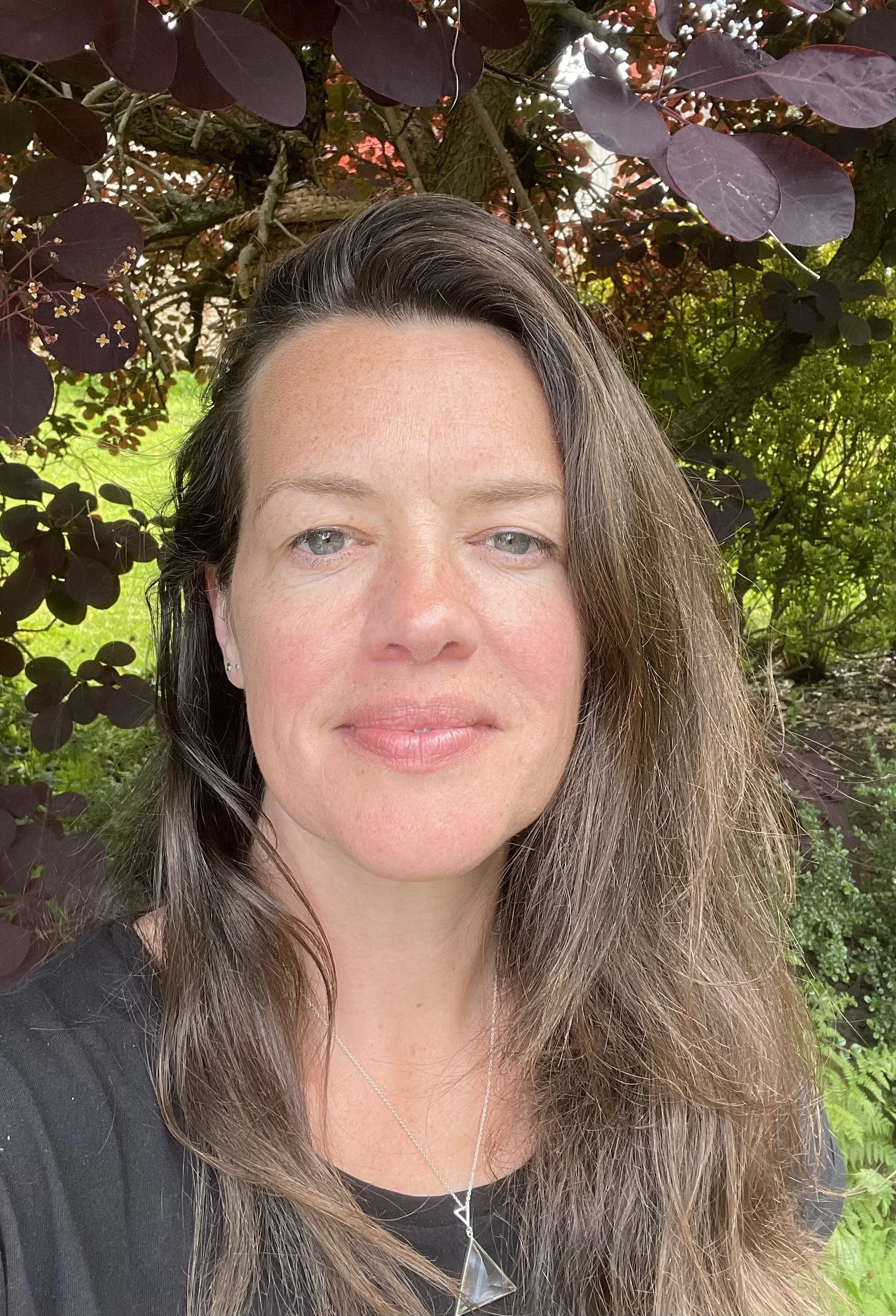 Photo of a white middle aged woman standing in a garden smiling