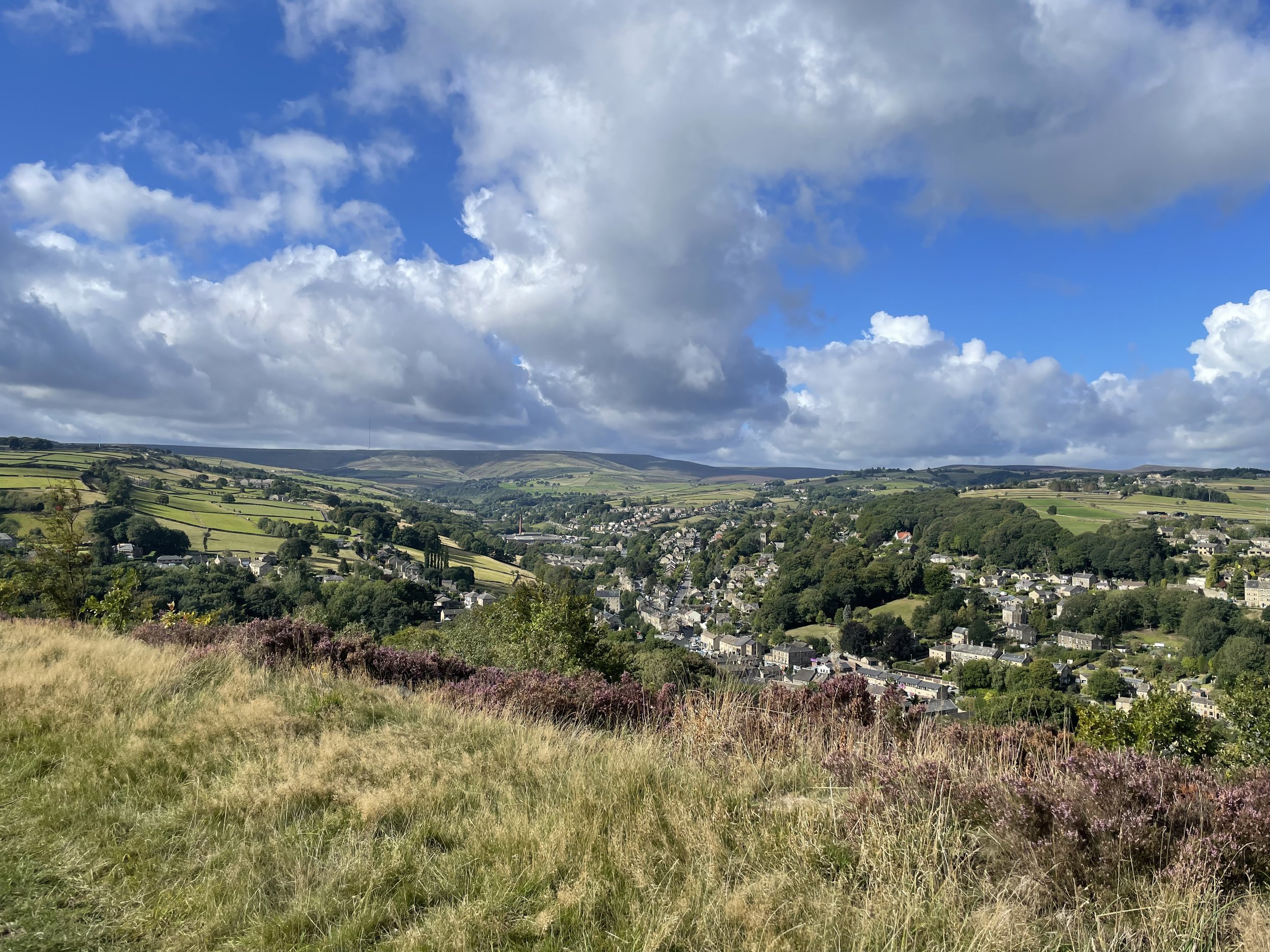 A broad landscape with a small town nestled among green hills under a partly cloudy sky.