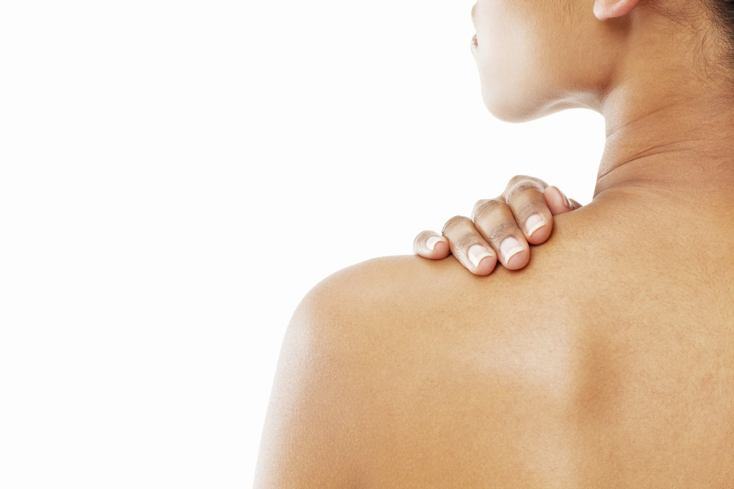 Close-up of a woman touching her shoulder with her hand, showing smooth skin and a neutral background.