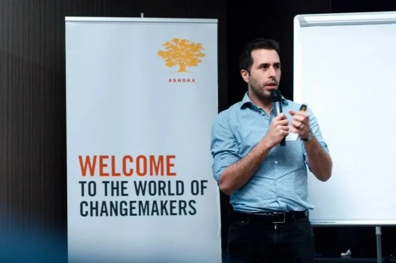 A man in blue shirt talks into microphone during a presentation