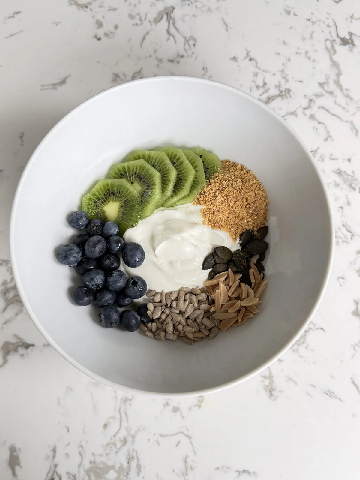 Greek yoghurt breakfast bowl with kiwi, blueberries, pumpkin seeds, almonds, sunflower seeds and ground flax.