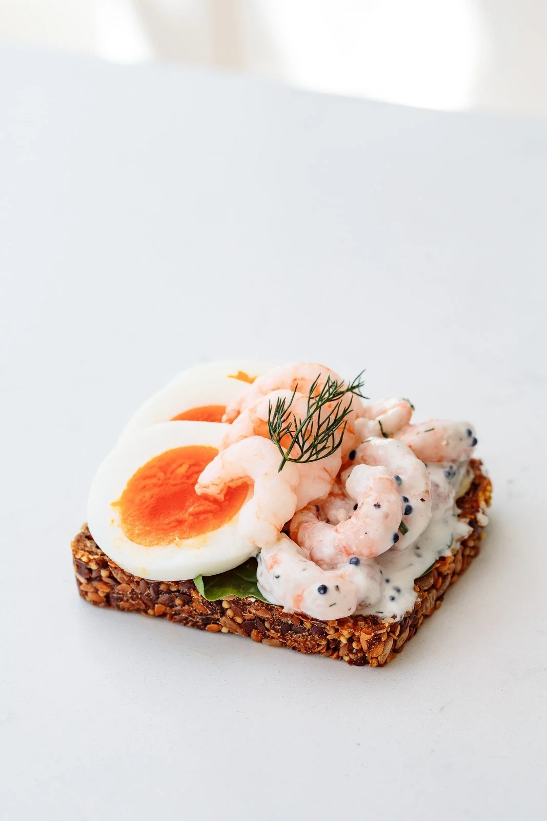 An open egg and shrimp sandwich on dark rye bread, topped with dill.