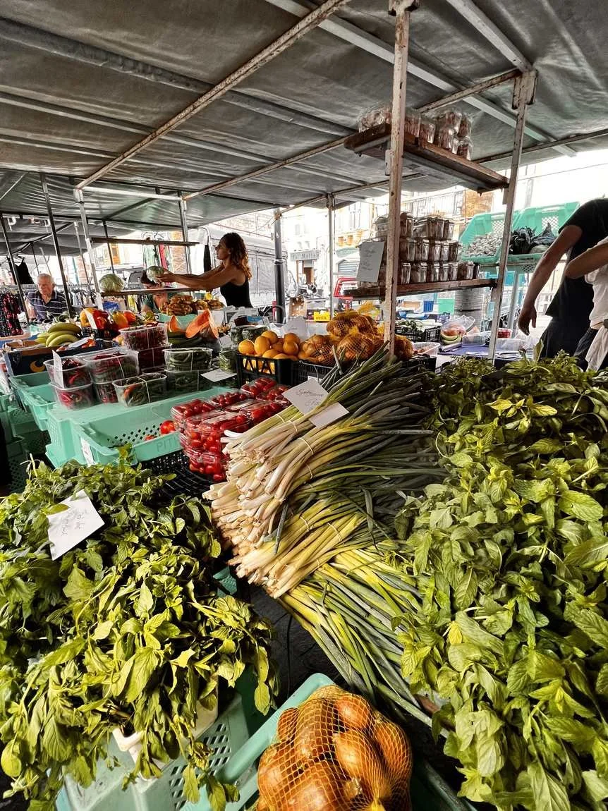 A busy farmers' market stall with fresh herbs, spring onions, tomatoes and seasonal fruit and vegetables.