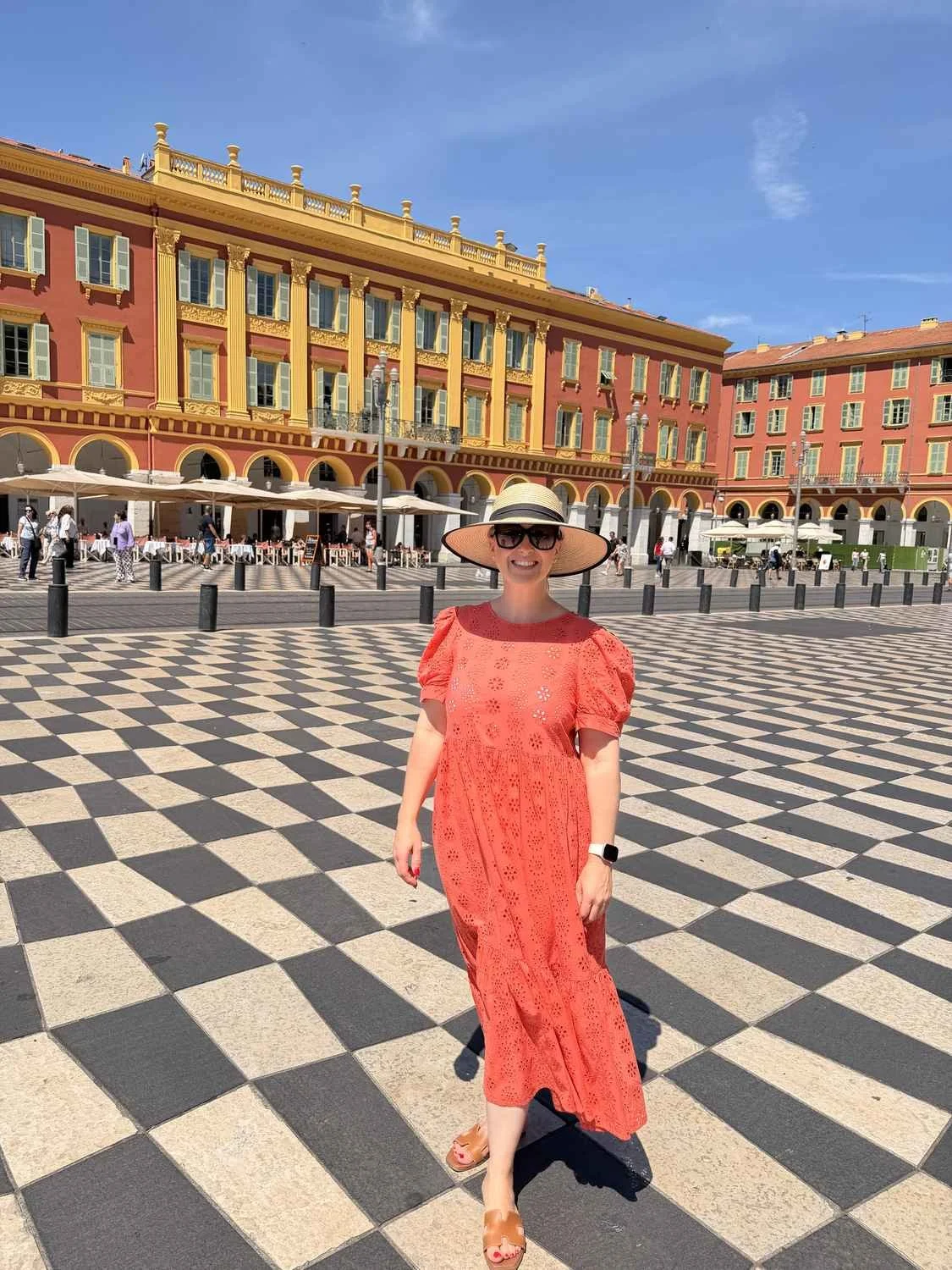Faye Palmqvist in Place Masséna, Nice, in a coral dress and straw hat.