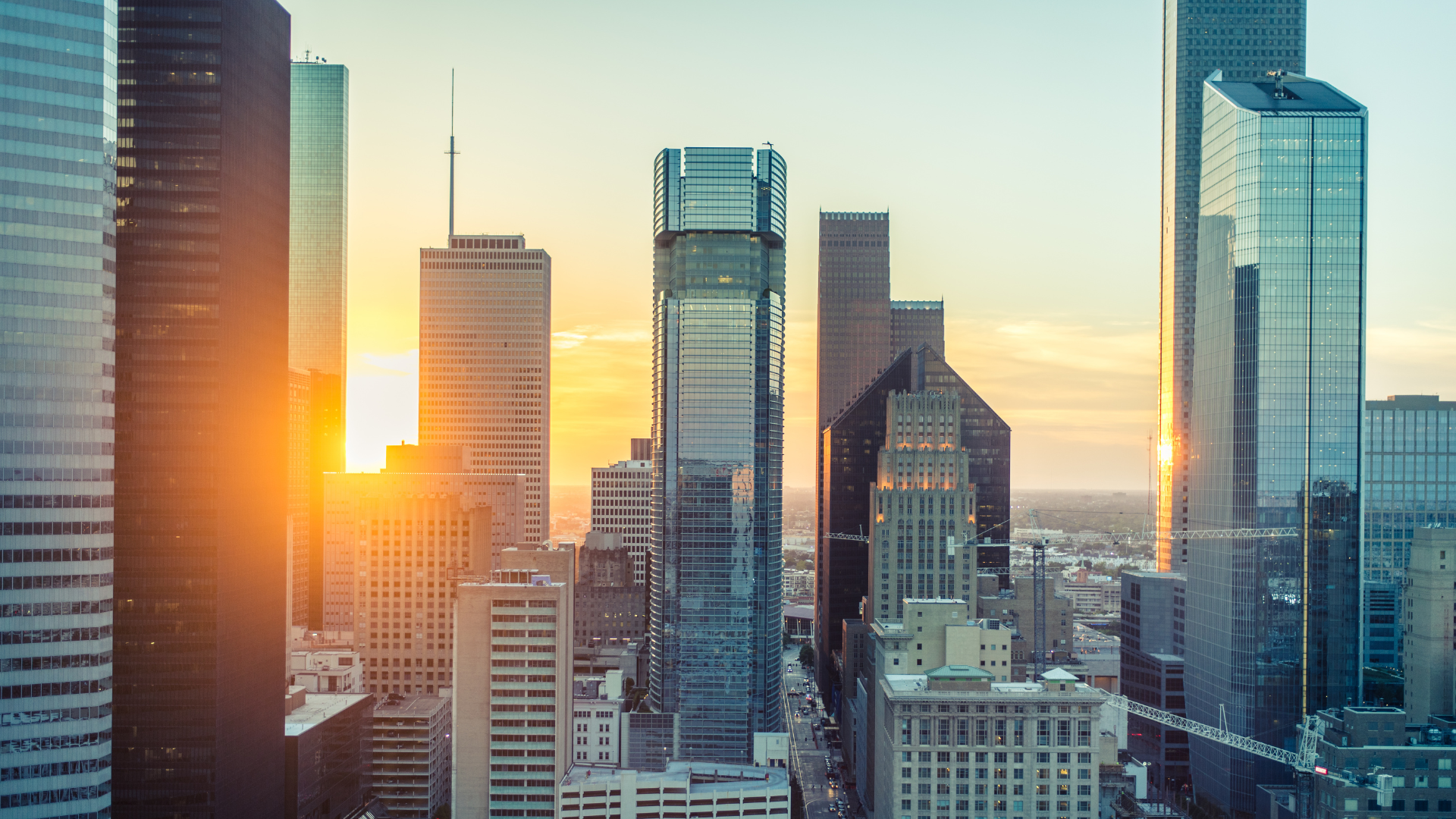 Sunset over a city skyline with tall modern glass skyscrapers reflecting the sunlight.