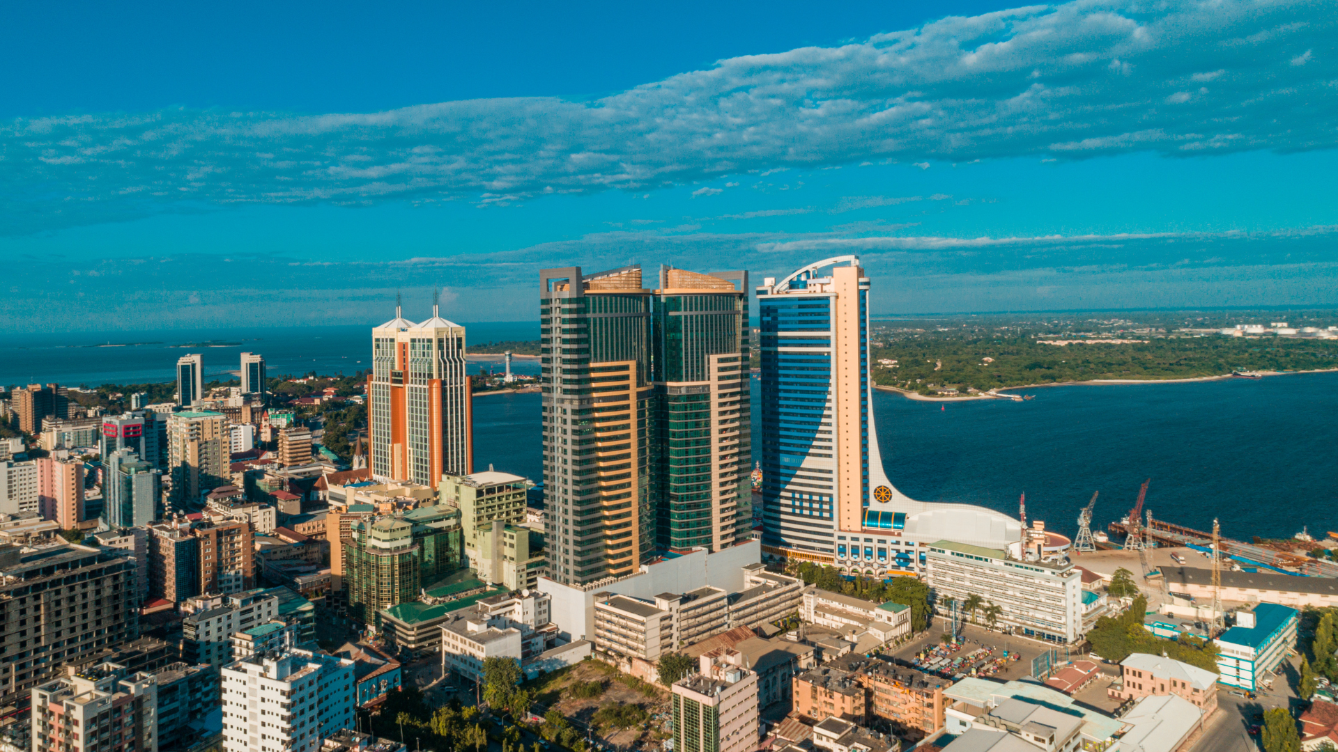 Aerial view of a city skyline with several tall modern buildings near a body of water, with a partly cloudy sky overhead.