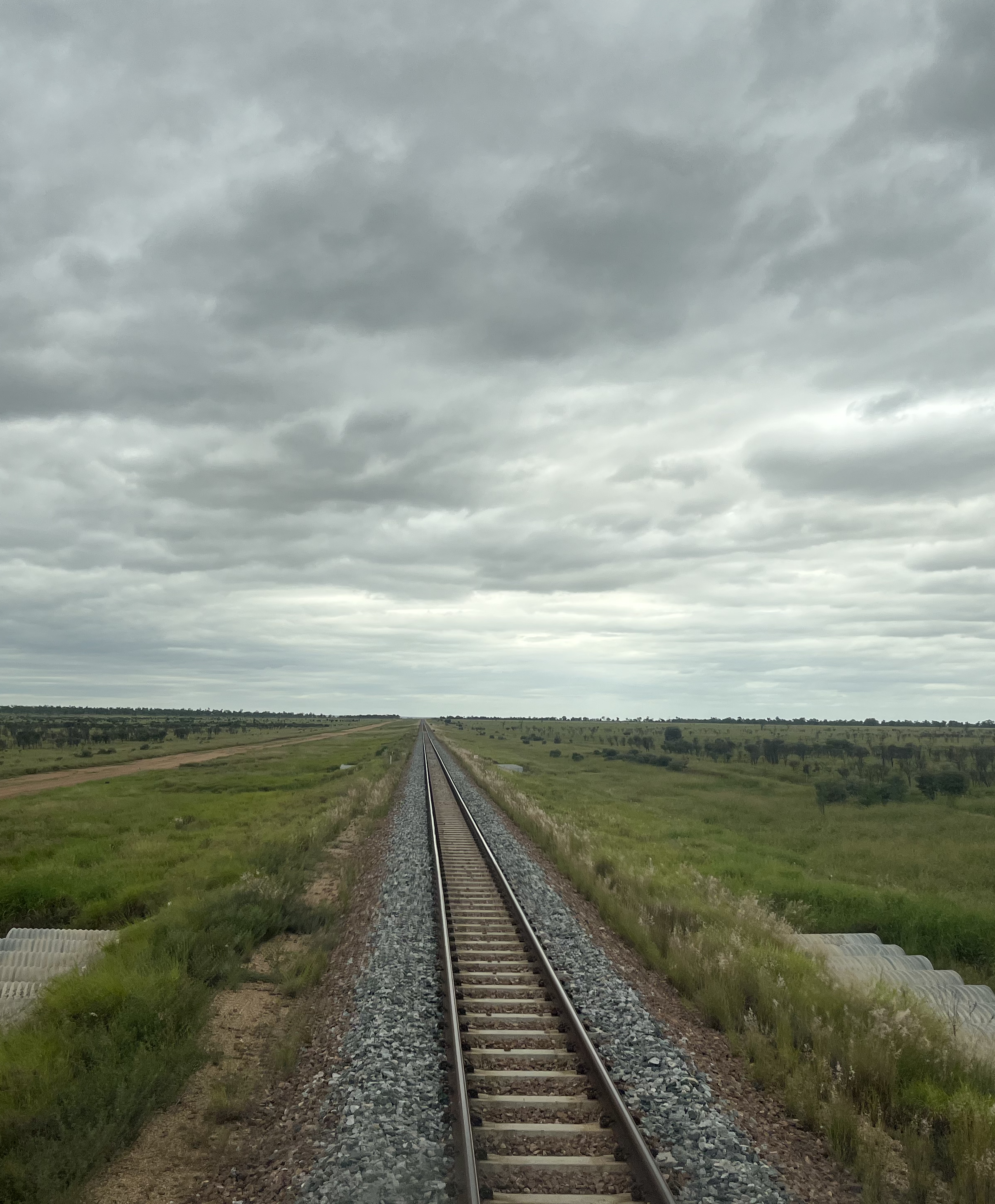A straight railway track running through a green countryside under a cloudy sky.