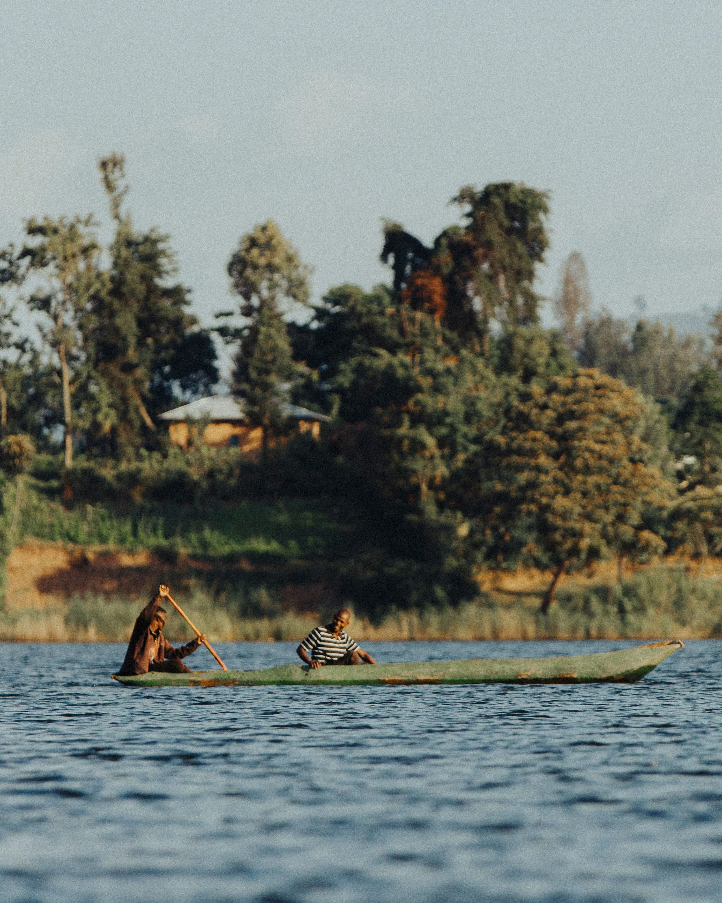 Dos personas en un kayak en un río, rodeadas de vegetación y árboles en el fondo, en un ambiente natural y tranquilo.