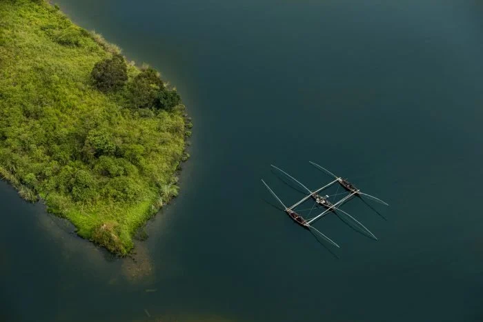 Vista aérea de un lago con dos botes de remo y una isla cubierta de vegetación a la izquierda.