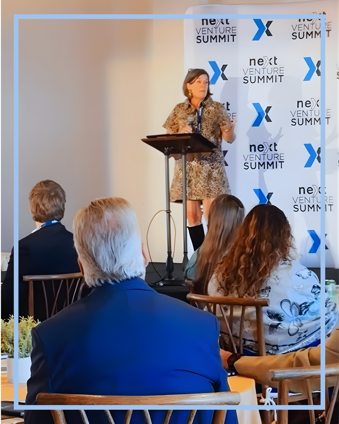 Caroline giving a speech at a conference with a "Next Venture Summit" backdrop and an audience of professionals seated in front.