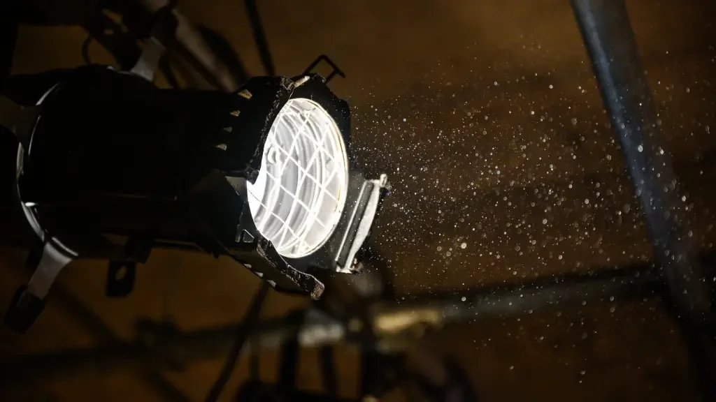 A stage light fixture projecting bright white light and creating dust particles visible in the air.
