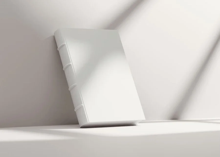 A white hardcover book resting on a white shelf against a white wall.