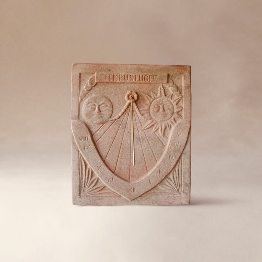 Pinkish decorative sundial with sun and moon faces, Roman numerals around the edge, and the words 'TEMPUS FUGIT' at the top.