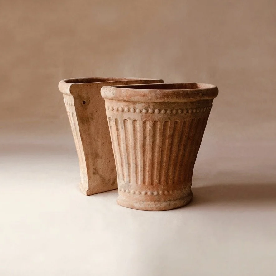 Two terracotta flower pots with decorative vertical ridges and dotted patterns, set against a plain background.