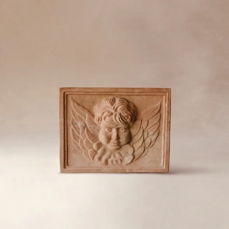 Terracotta carving of a cherubic face with wings, framed by a rectangular border