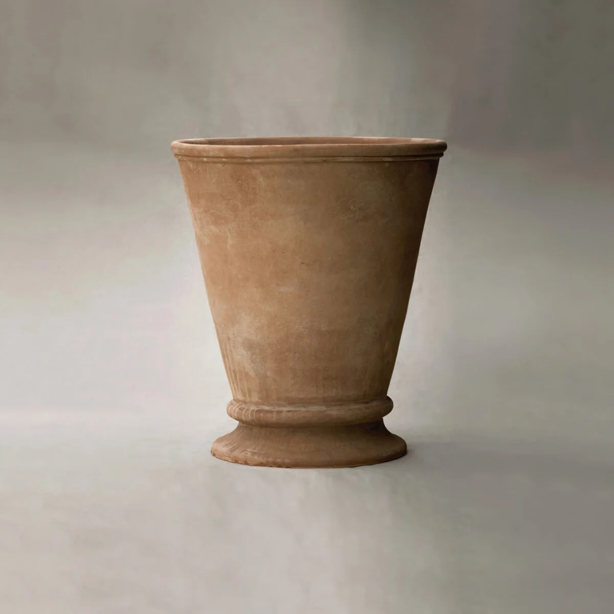 A plain, tall clay flower pot against a grayish background.