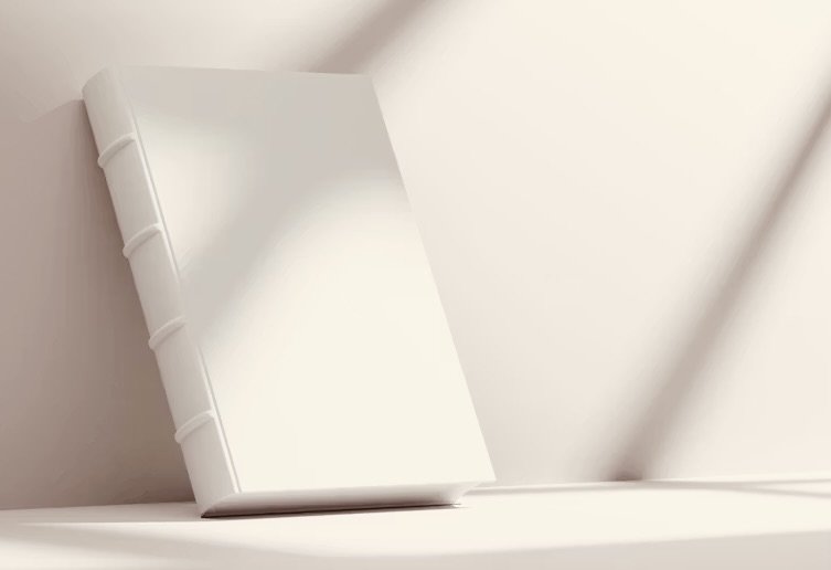 A white, closed hardcover book with a smooth cover, resting on a white surface against a white wall.