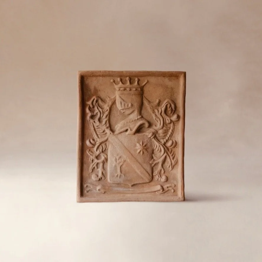 A rectangular terracotta-colored tile with a raised coat of arms featuring a shield, a crown on top, a ship above the shield, and decorative elements around it.