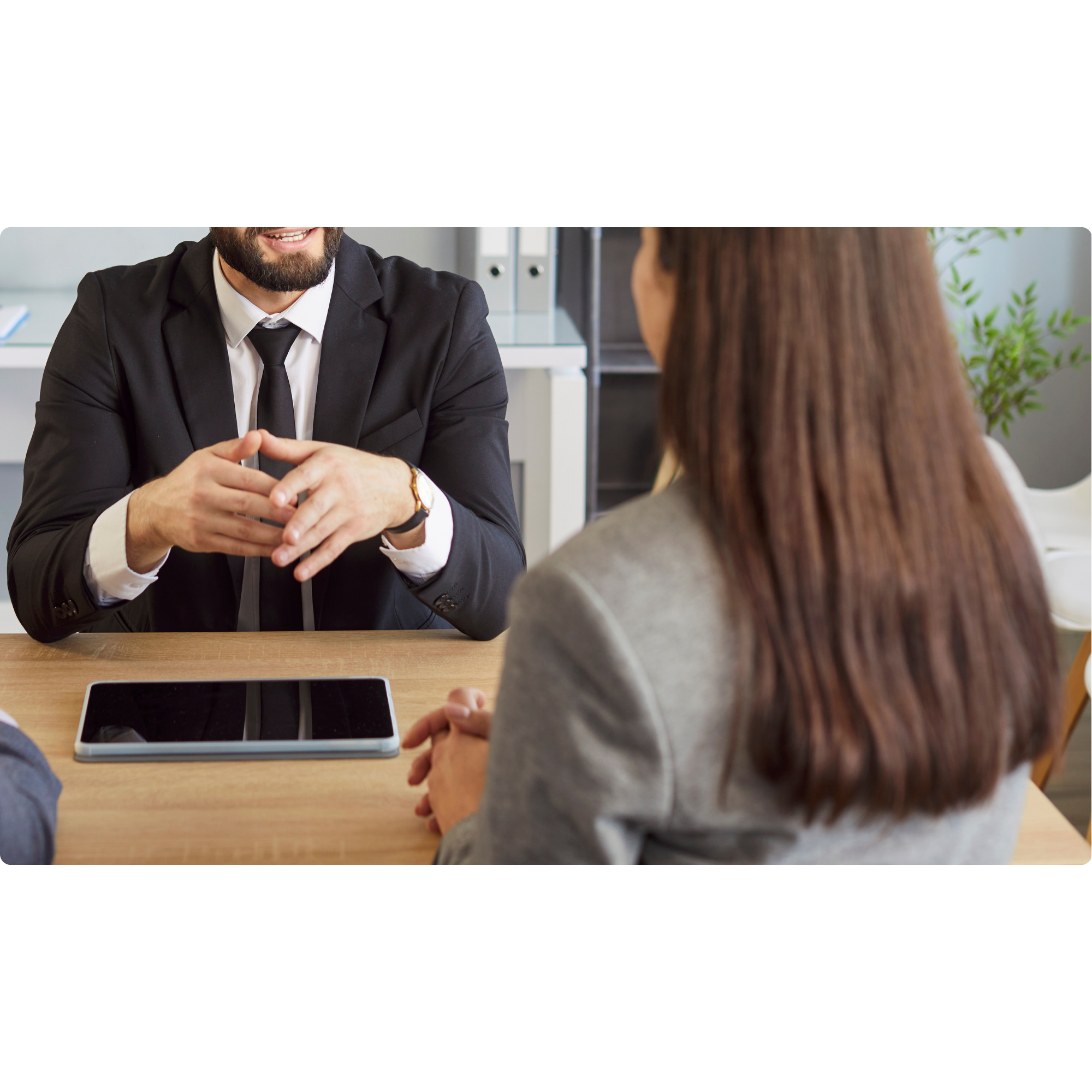 Man in black suit and woman in gray blazer having a business meeting at a desk, with digital tablet on the table.