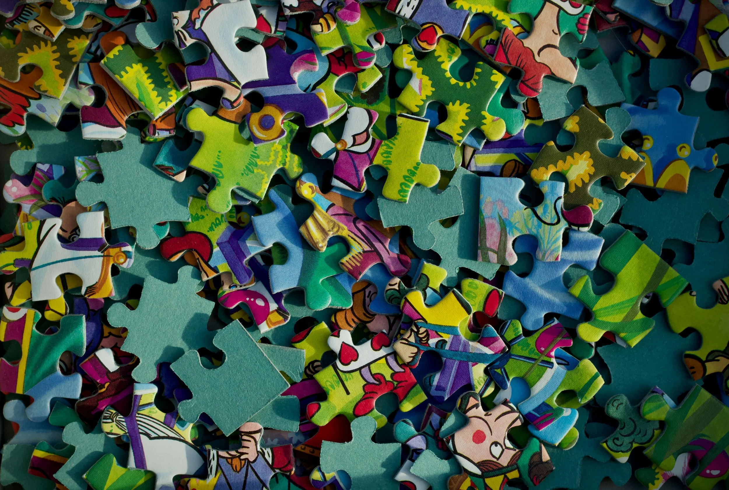 Colorful jigsaw puzzle pieces scattered and overlapping, with various bright, cartoonish patterns and illustrations.