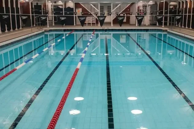 Indoor swimming pool with multiple lanes, lane dividers, and a spectator area in the background.