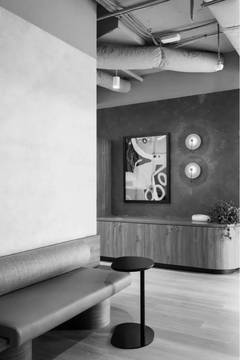 Empty modern lounge with a bench, a small round side table, artwork, wall-mounted lights, and a plant, in a stylish interior.