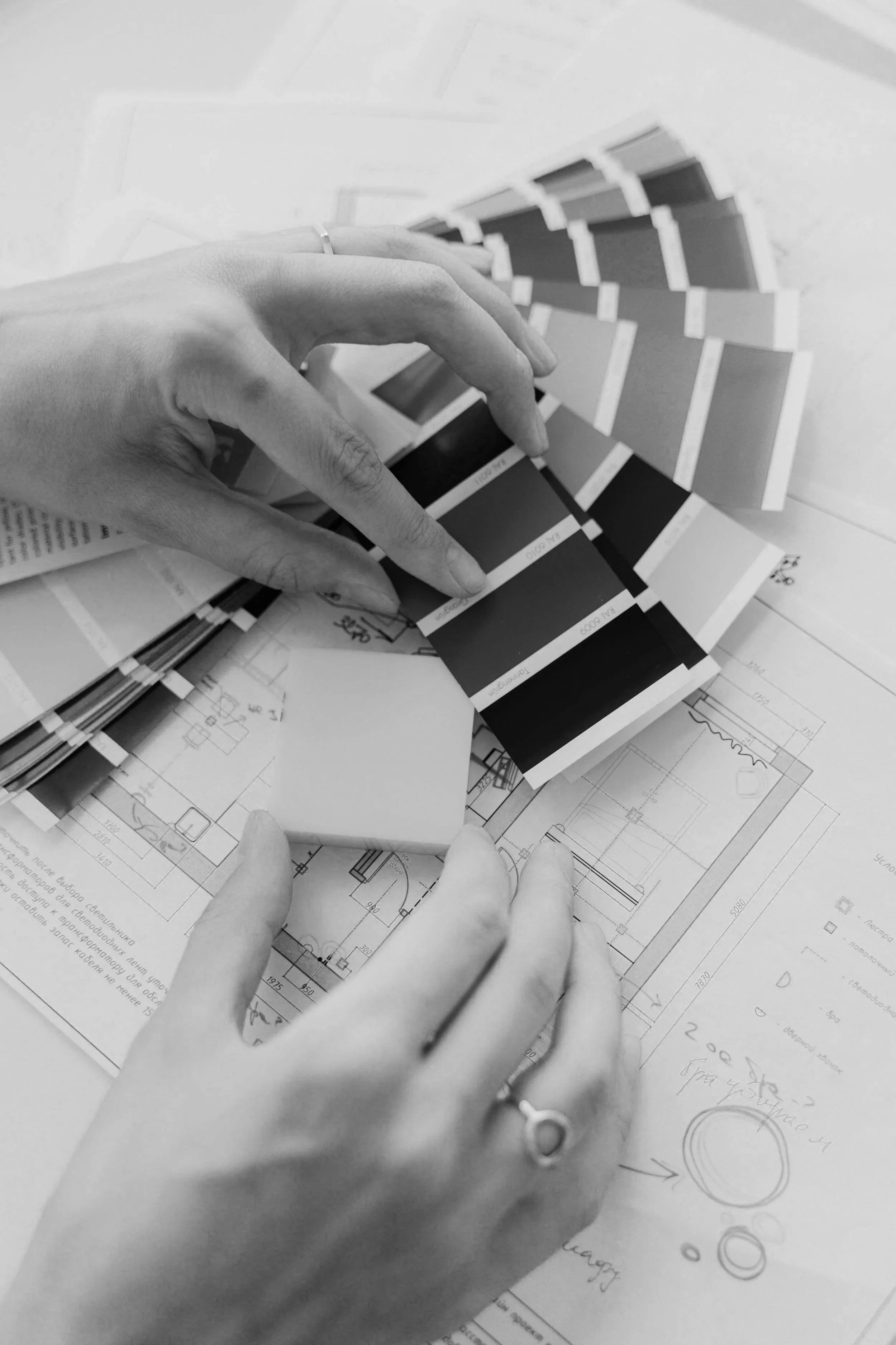 Black and white photo of hands reaching over architectural blueprints, with color swatches fanned out on top.