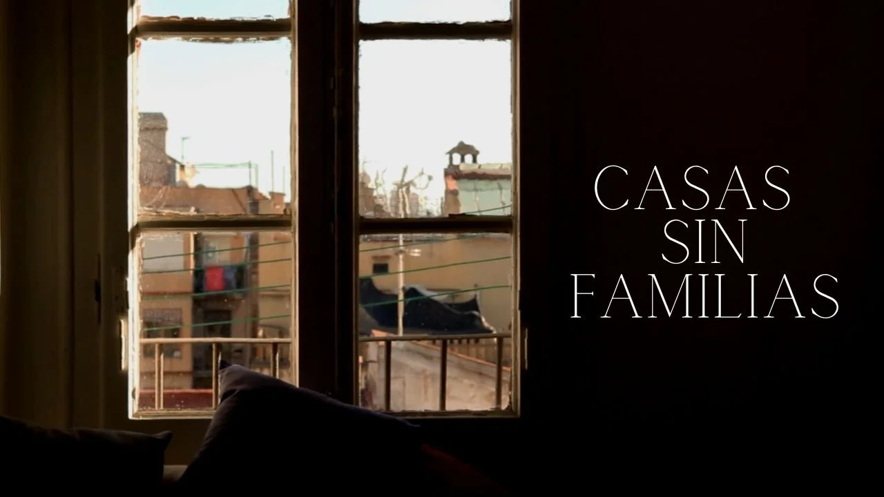 View through a window showing neighboring buildings and rooftops in an urban area with laundry hanging outside. Text overlay says 'Casas Sin Familias'. Poster for the documentary short Casas Sin Familias.
