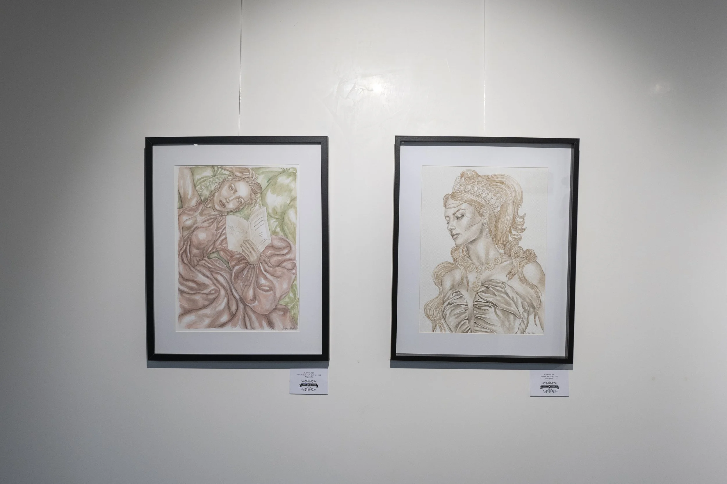 Deux dessins encadrés de femmes, exposés sur un mur blanc, dans une galerie d'art.