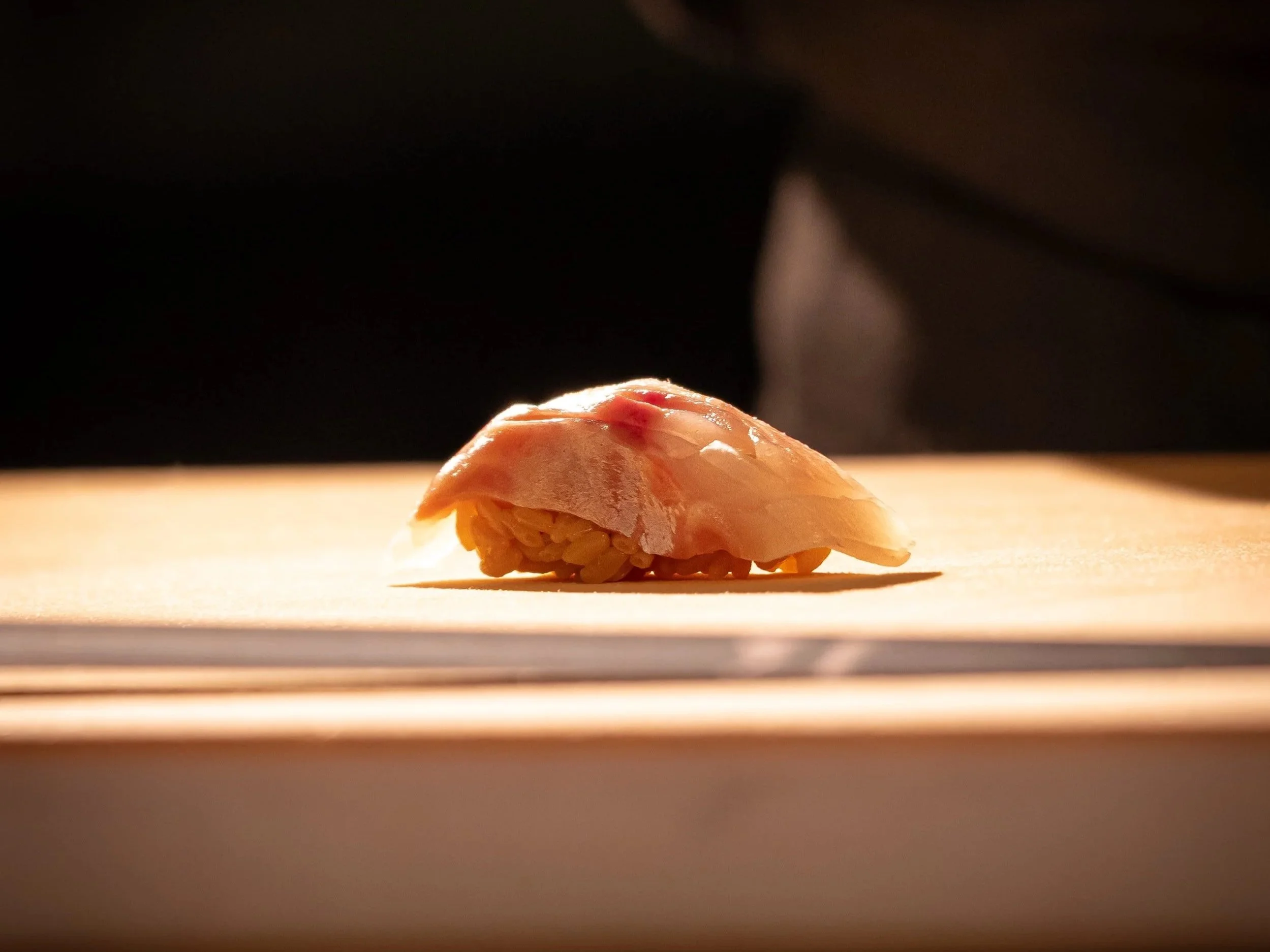 A piece of nigiri sushi with a slice of raw fish on top of rice, placed on a wooden surface.