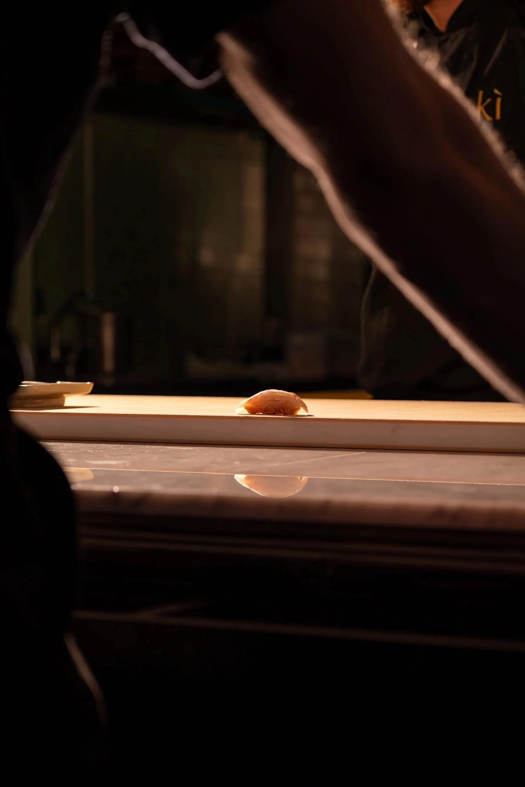 A piece of raw salmon placed on a wooden sushi rolling mat, illuminated by warm light, with a blurred background.