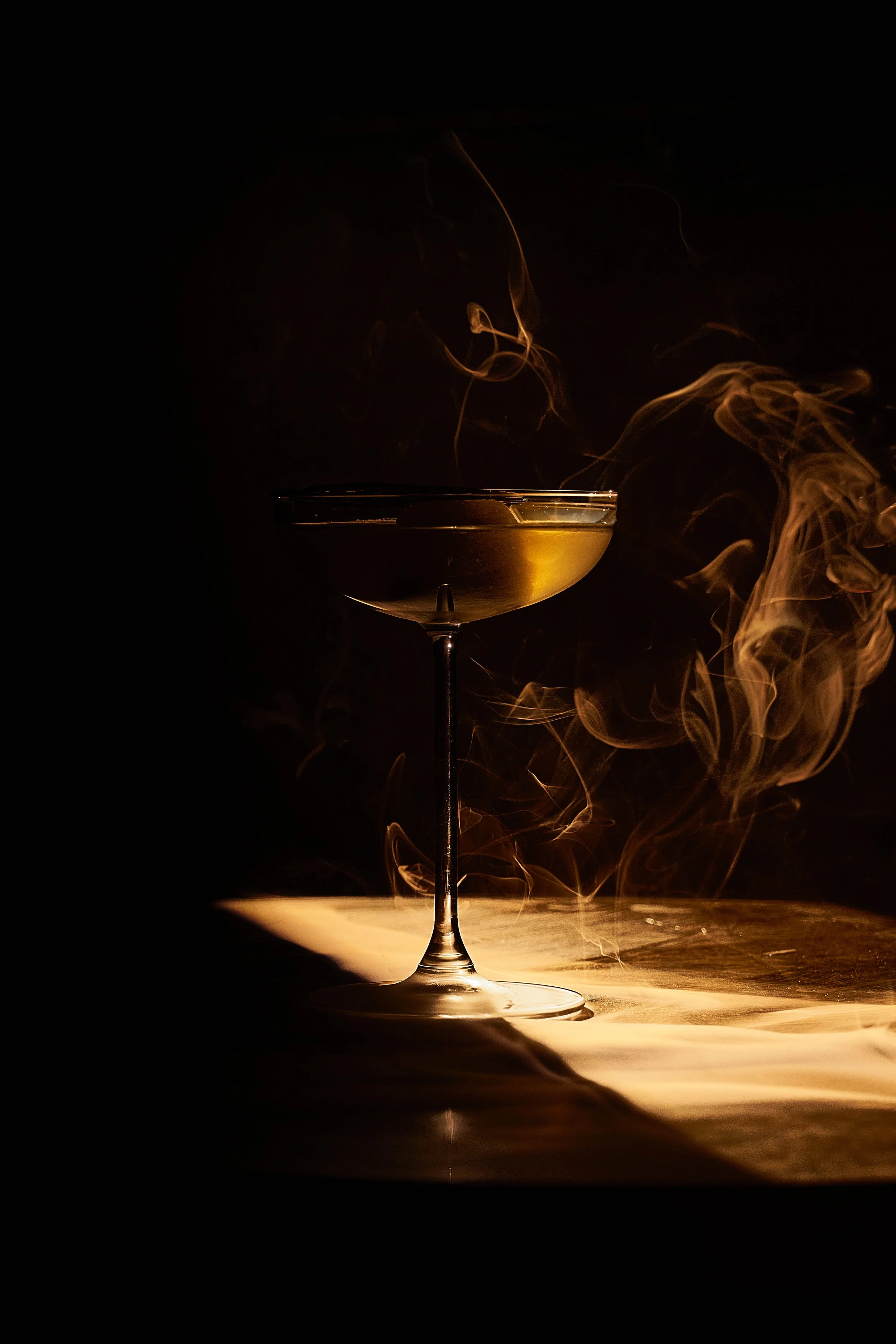 A cocktail glass with a drink and swirling smoke or vapor against a dark background.