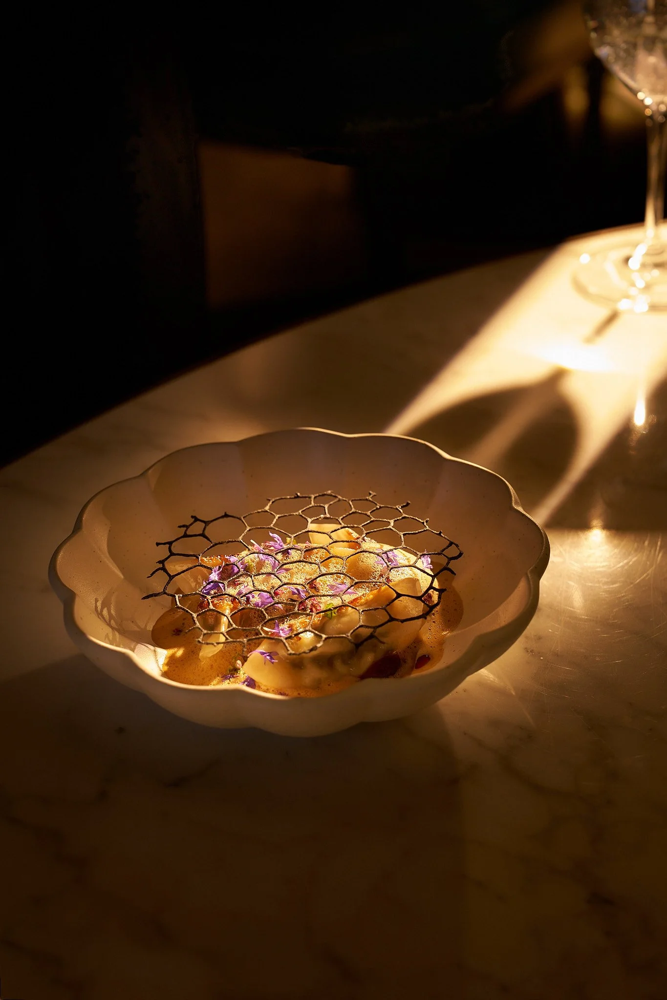 A plated dish with food garnished with edible flowers, served under warm lighting on a dark background.