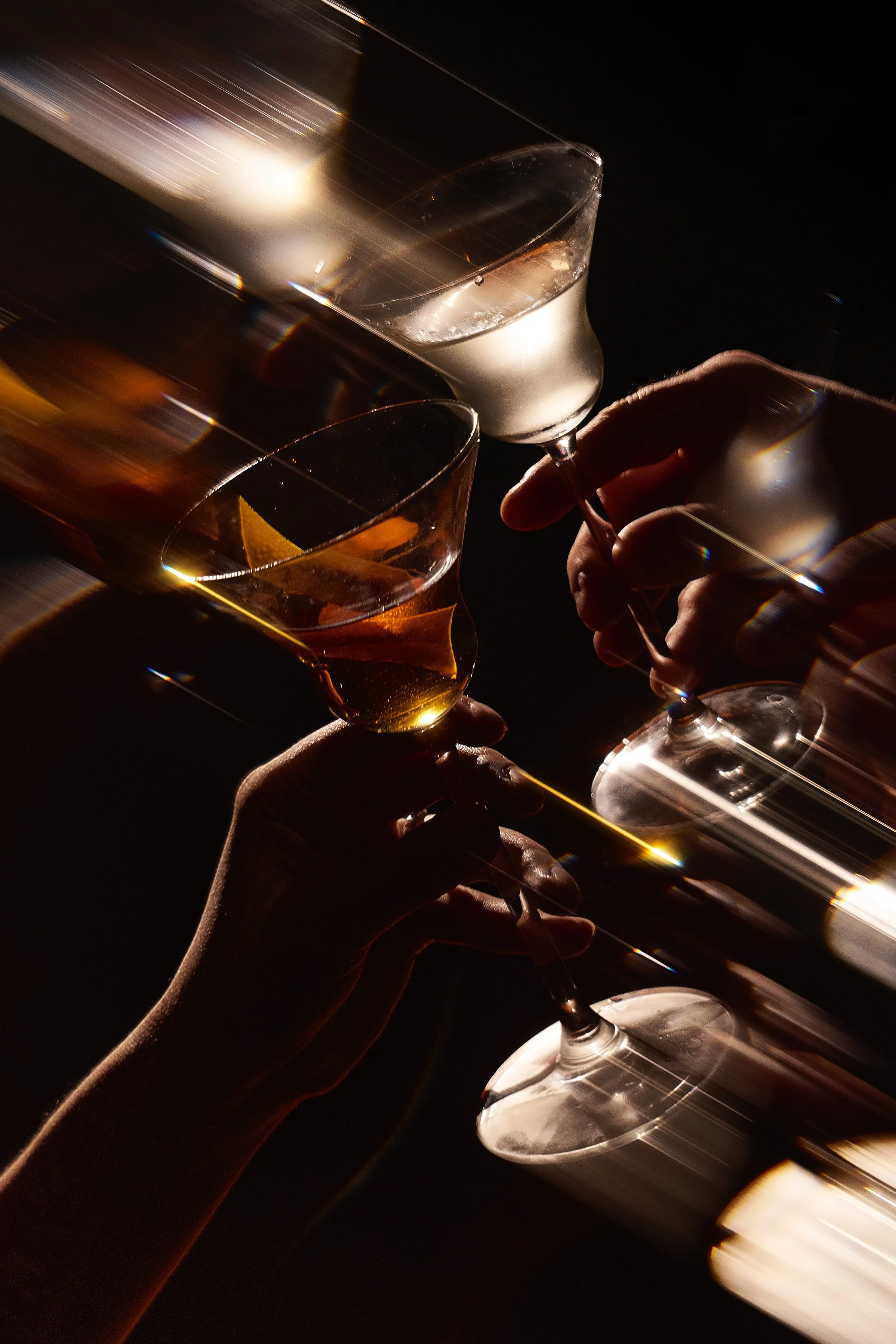 People holding glasses of champagne and wine in a toast, with a dark background and artistic lighting effects.