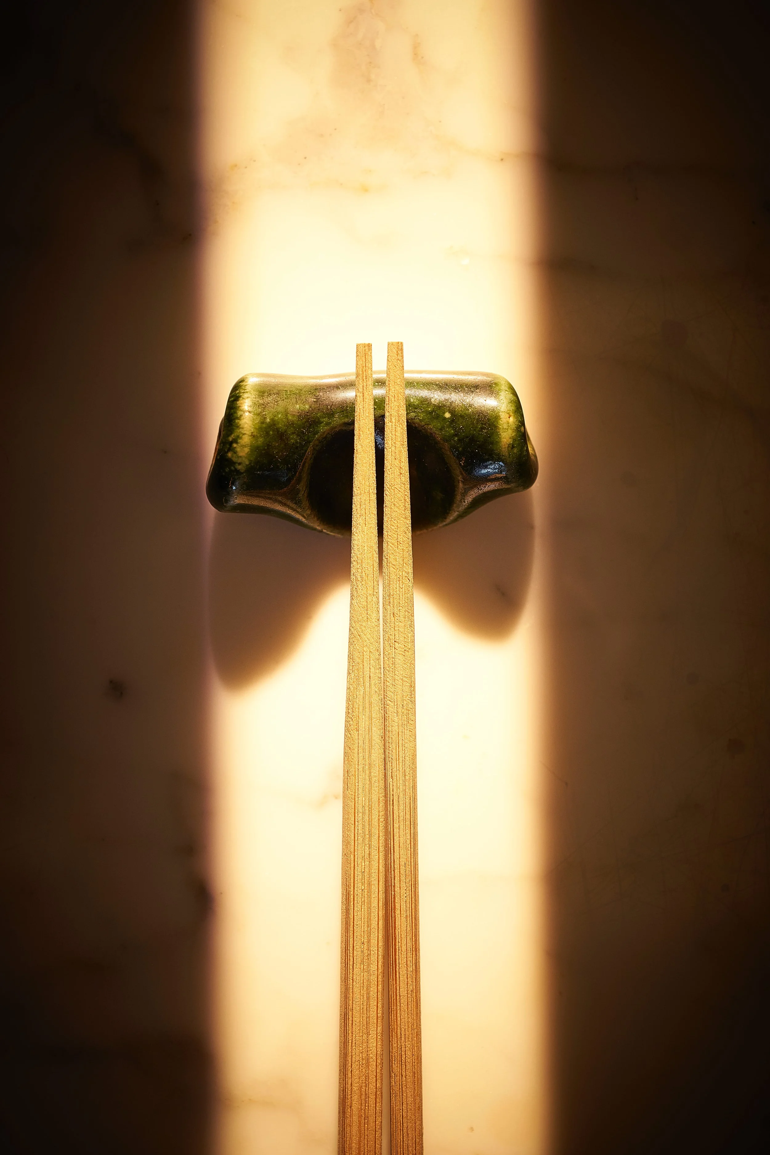 Chopsticks resting on a ceramic chopstick holder, with sunlight creating shadows.