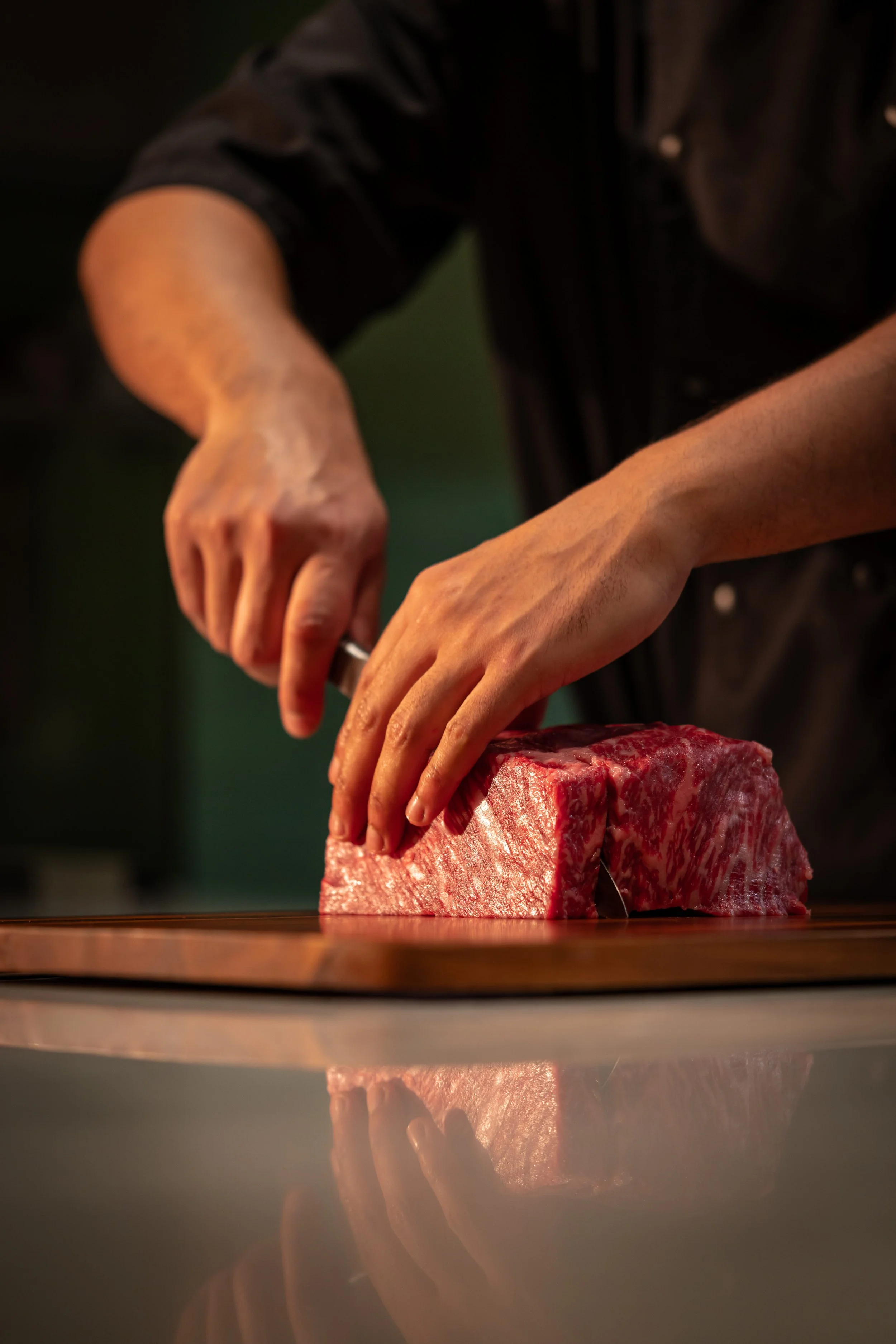 A chef slicing a large, high-quality piece of marbled beef on a wooden cutting board.