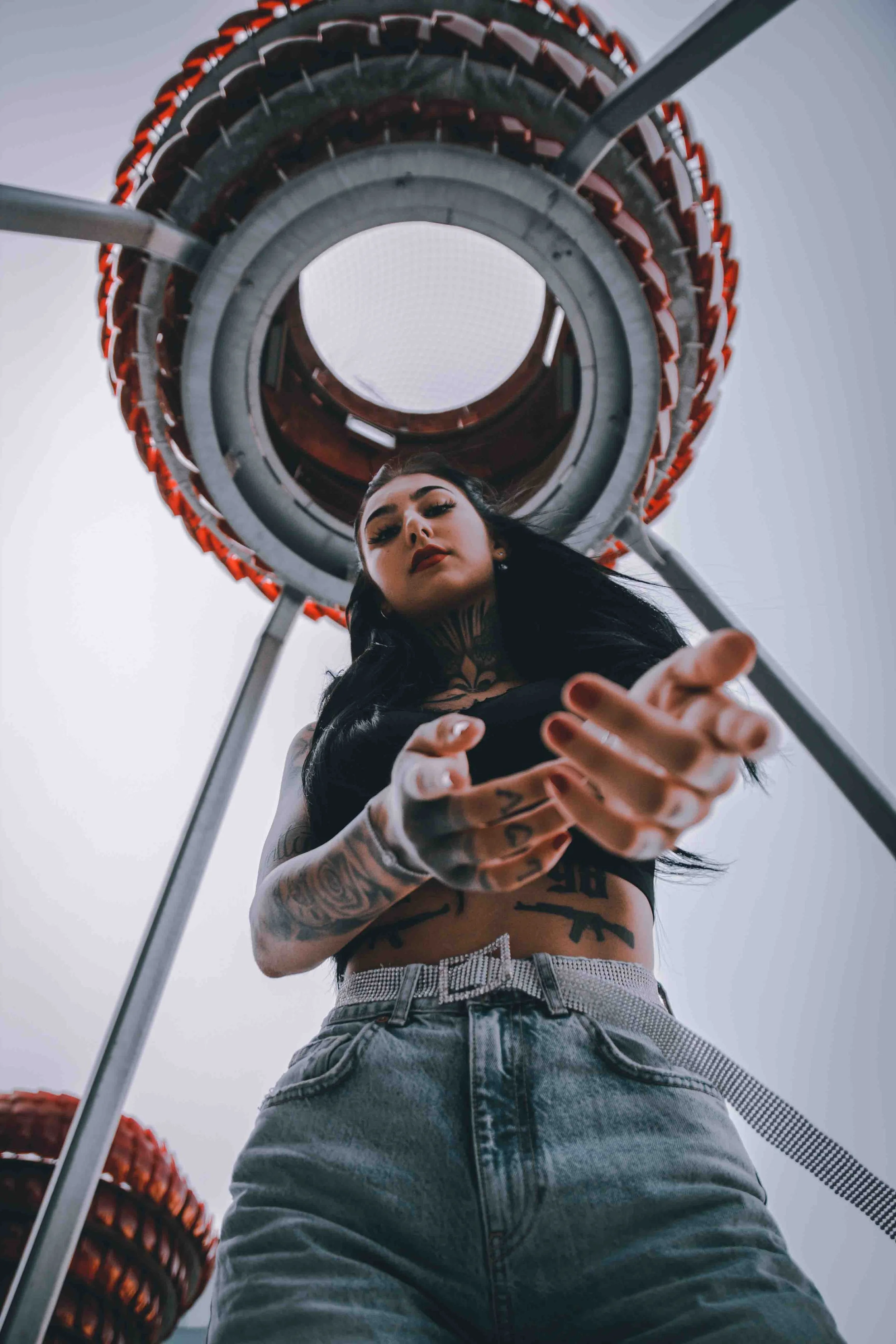 Frau mit Tattoos blickt nach unten, fotografiert von unten mit einer Achterbahn im Hintergrund.