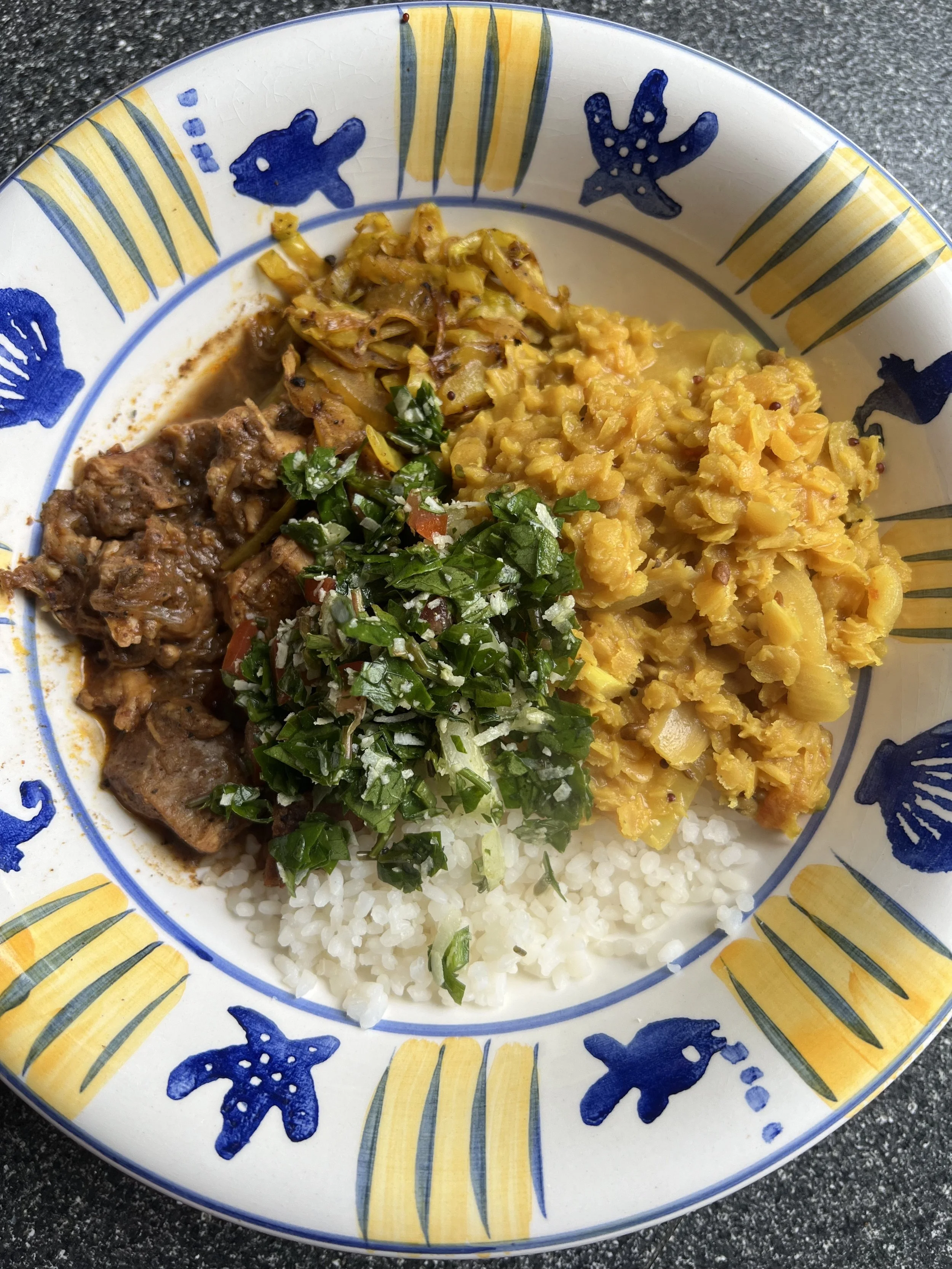 Plate of food with rice, cooked vegetables, meat stew, and chopped greens, on a decorated blue and yellow patterned plate.