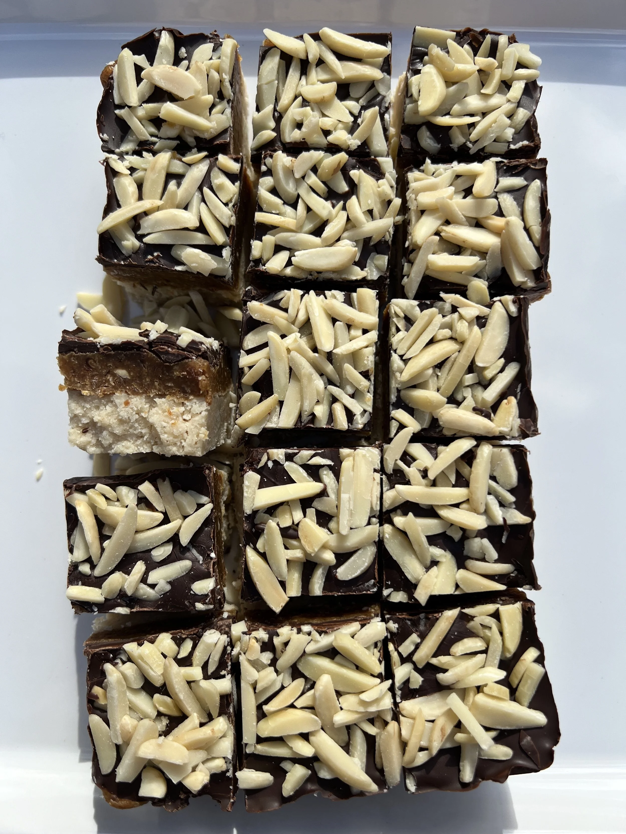 Assorted chocolate topped with sliced almonds, arranged in a grid pattern on a white tray.