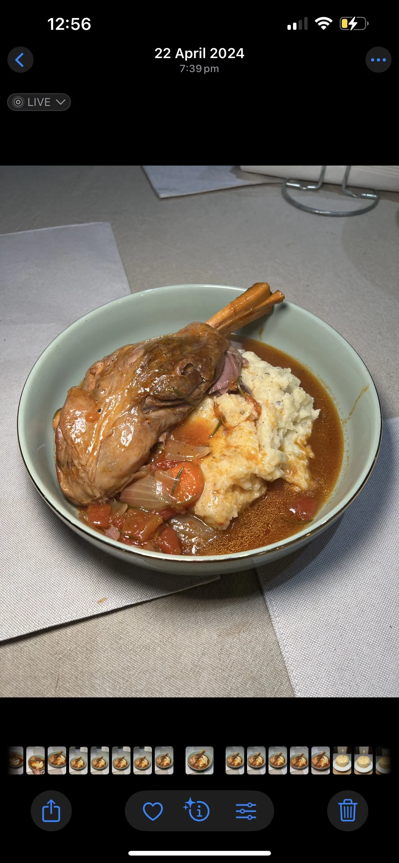 A bowl of food containing a large piece of cooked lamb shank, mashed potatoes with gravy, and a stew with vegetables like carrots and onions.