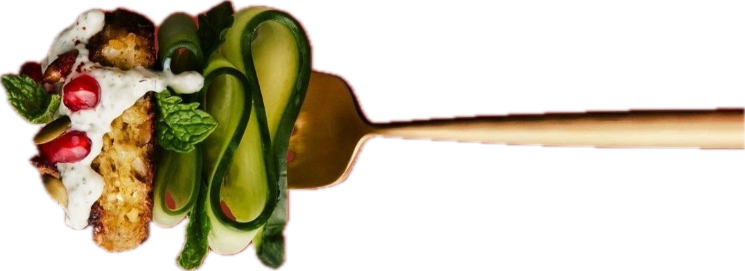 A fork with cucumber slices, pomegranate seeds, and a mint leaf on the left, with a dessert topped with whipped cream, pomegranate seeds, and mint toward the top left.