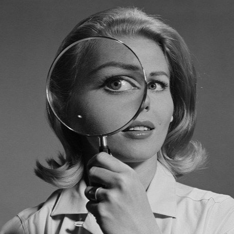 A woman with styled hair looking through a magnifying glass.