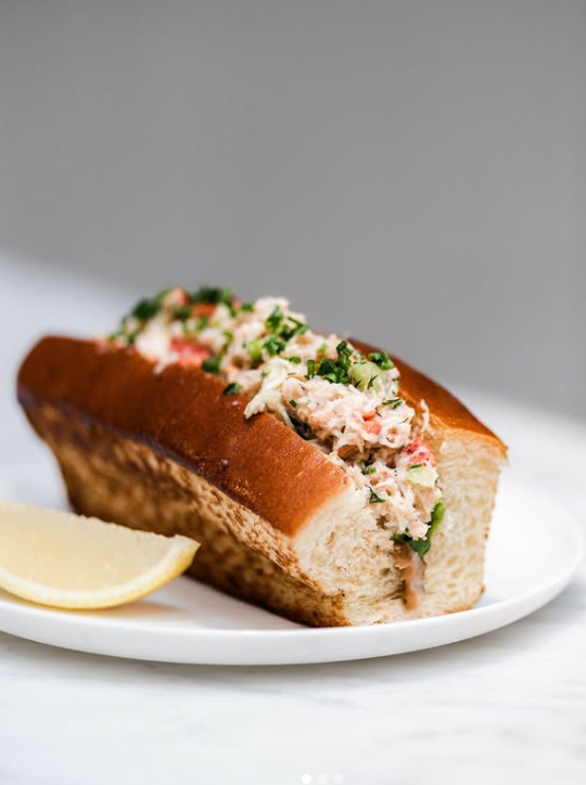 Lobster roll with a lemon wedge on a white plate.