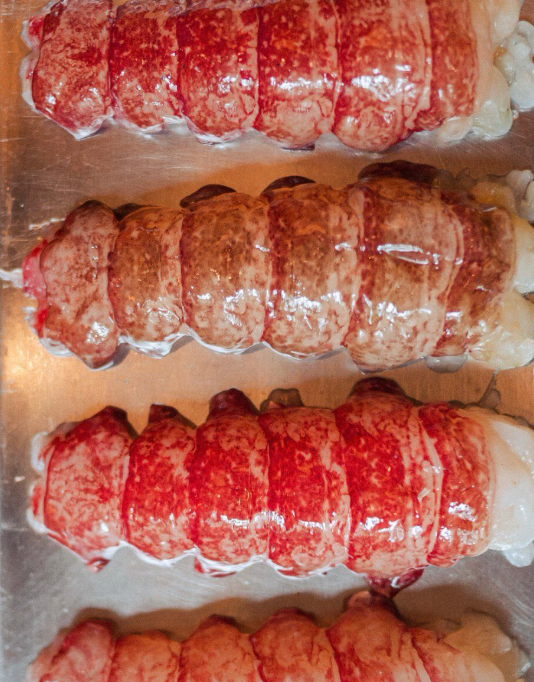 Close-up view of four lobster tails on a baking sheet, ready for cooking.