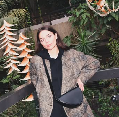Young woman in a blurry photo, standing outdoors with lush green plants surrounding her.