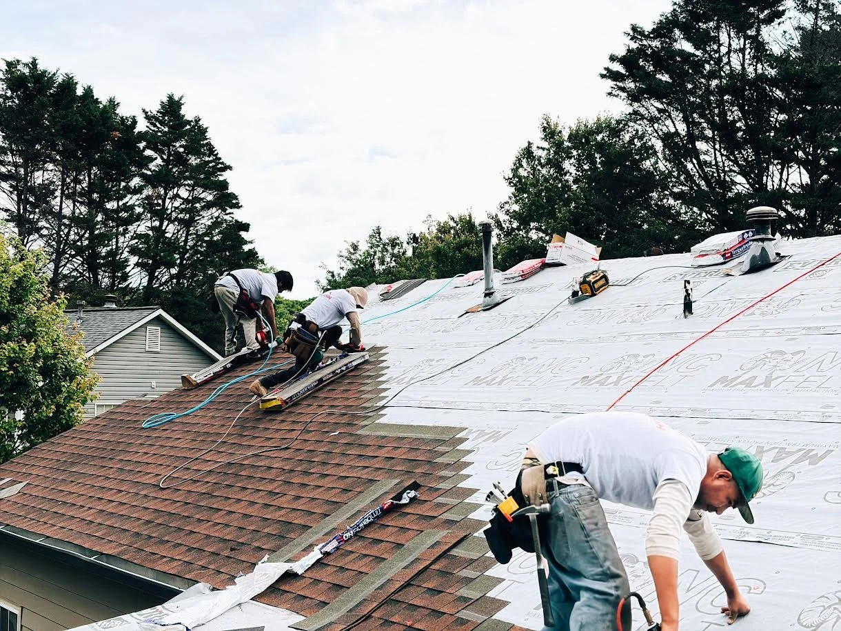 Workers installing roofing on a house, with some sections covered in underlayment and others with shingles in progress.