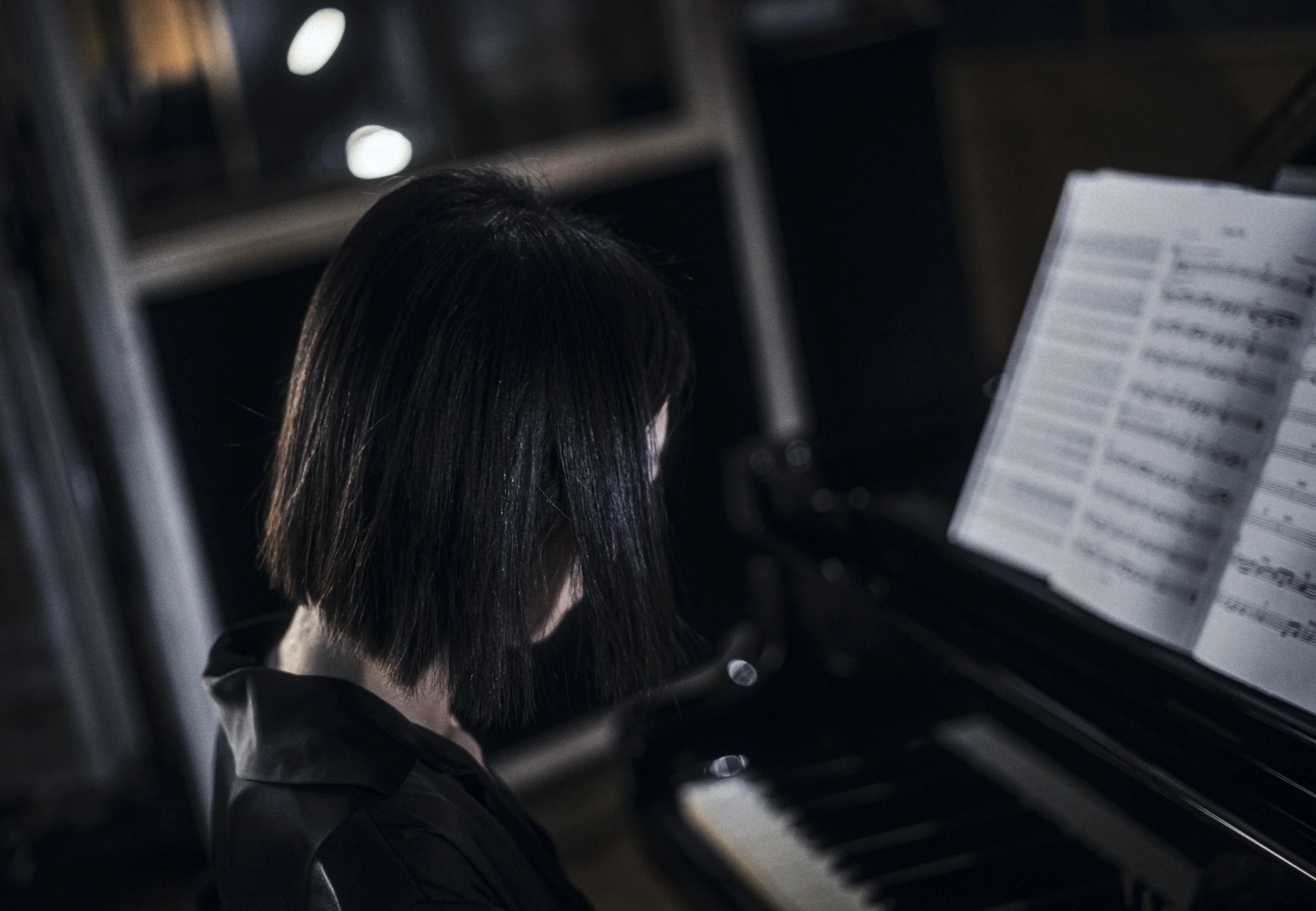 A person with black hair playing the piano with sheet music in front of them.