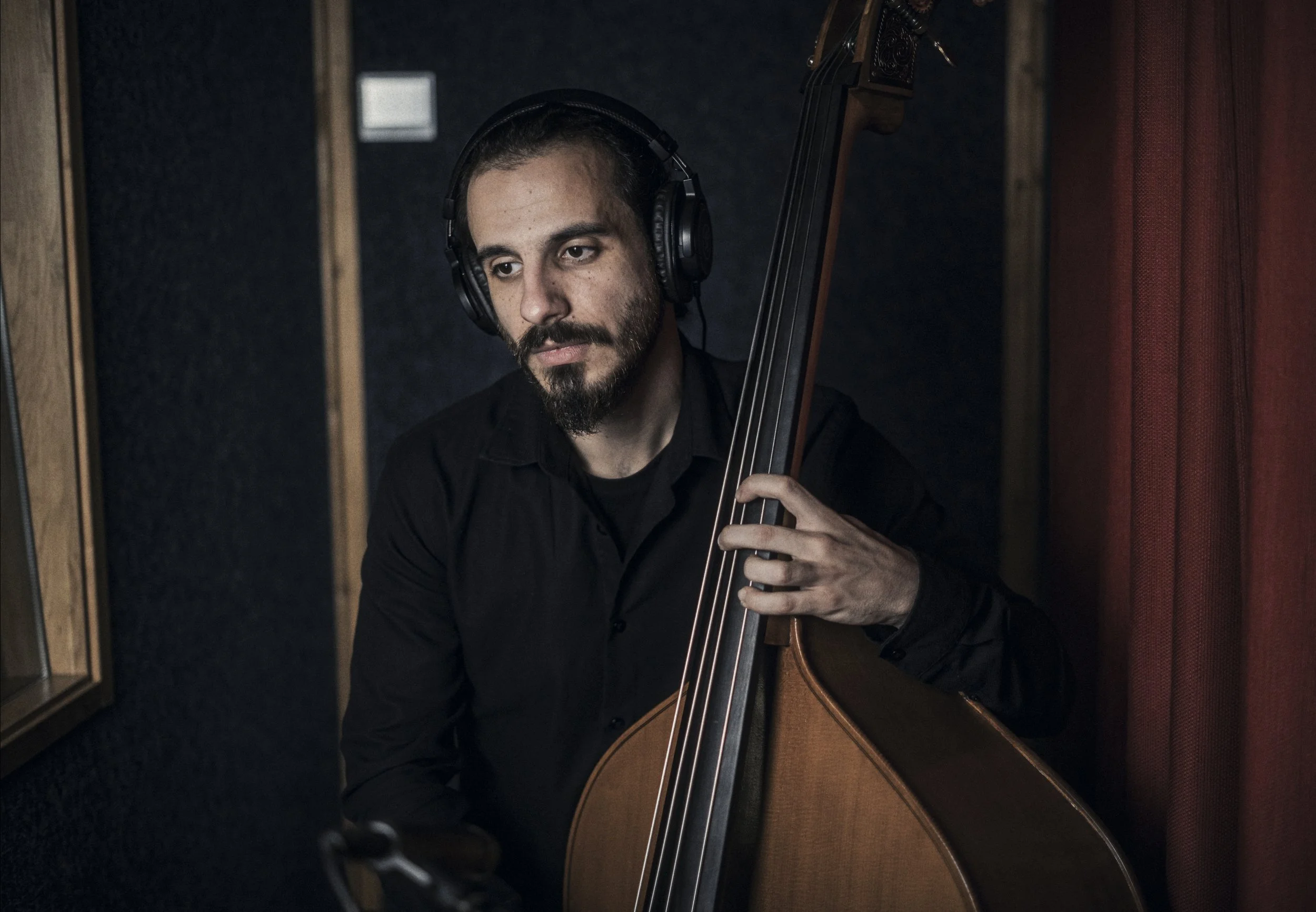 Man with beard wearing headphones playing double bass in recording studio.