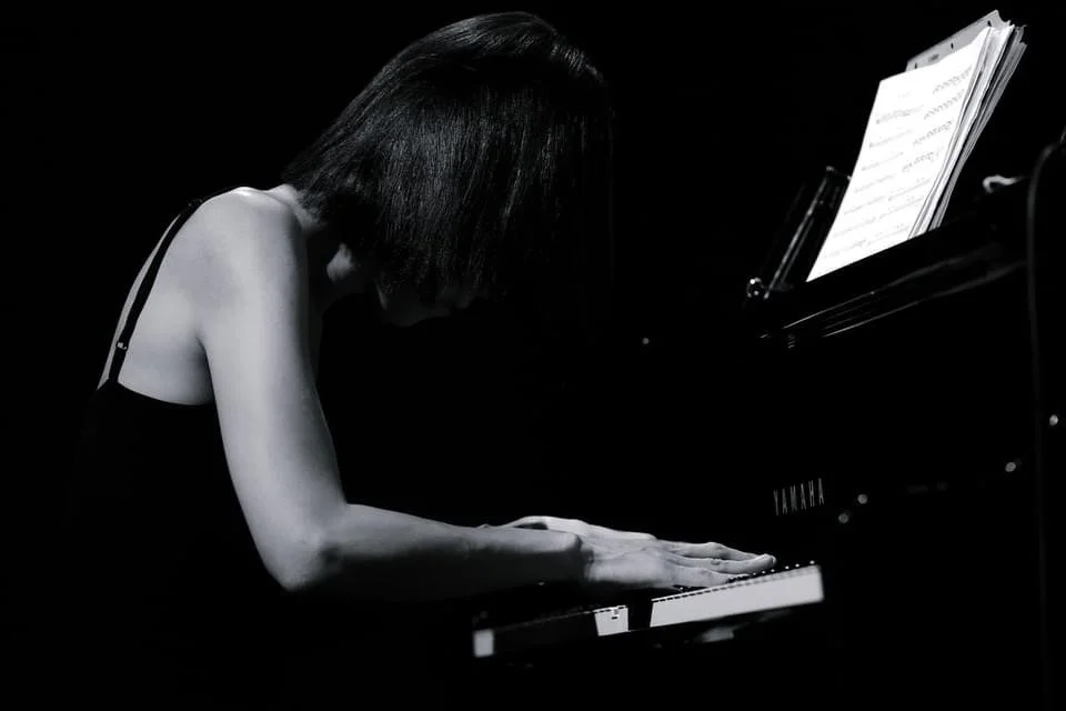 A woman playing the piano in a dark setting, with sheet music on the stand.