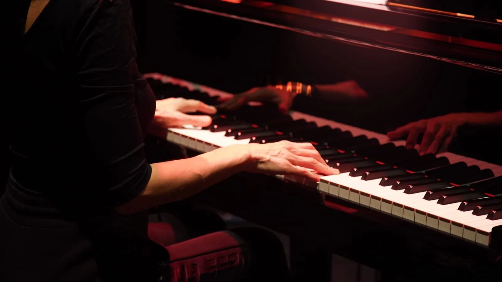 A person playing a piano in a dimly lit setting with red lighting.